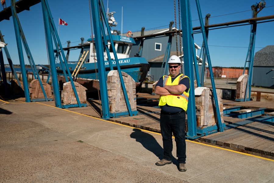 A person in a yellow vest and white helmet standing in front of blue metal structuresAI-generated content may be incorrect.
